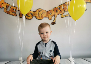 Chłopiec siedzi na tle fotograficznym i pozuje do zdjęcia wśród balonów.